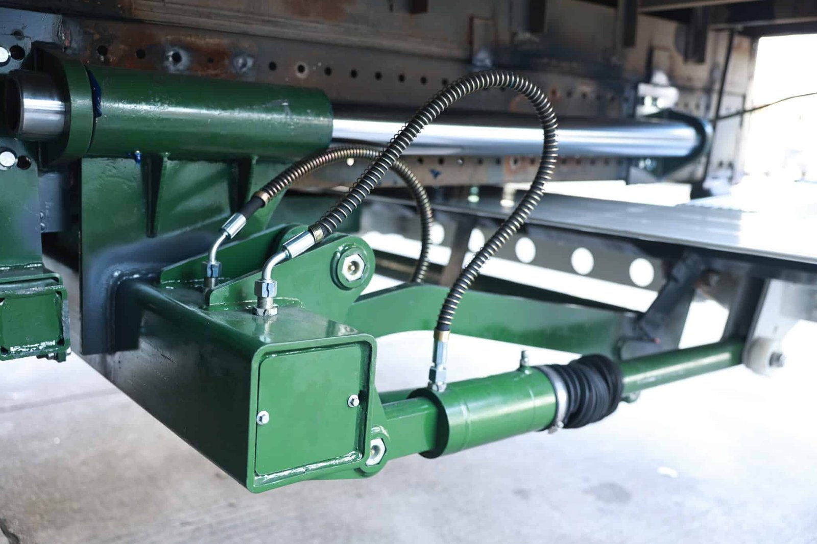 Close-up of a hydraulic tail lift pump unit, hoses, cylinders, and reinforced mounting points on a refrigerated truck